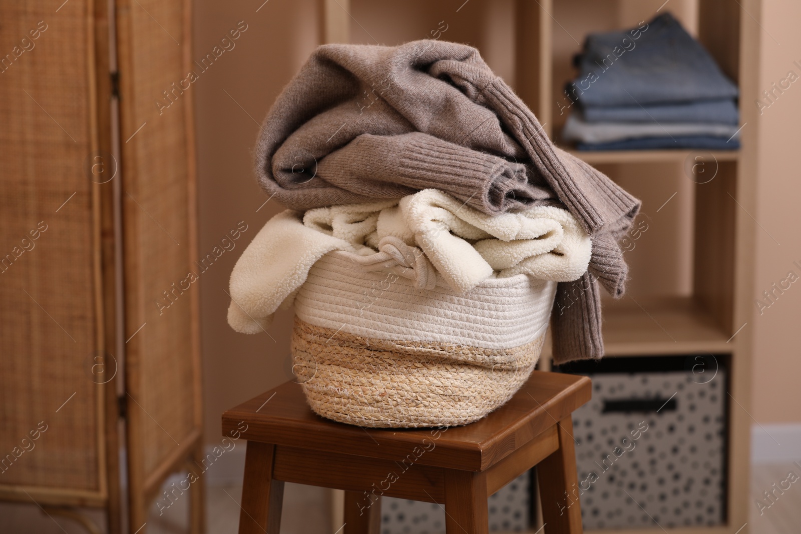 Photo of Wicker laundry basket overfilled with clothes on wooden stool indoors