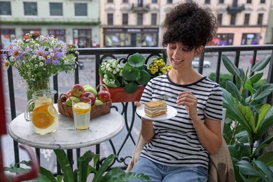 Photo of Young woman eating piece of cake on balcony with beautiful houseplants