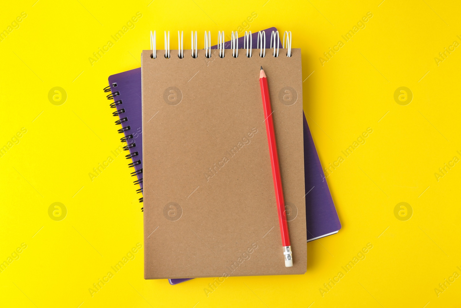 Photo of Notebooks with pencil on yellow background, top view