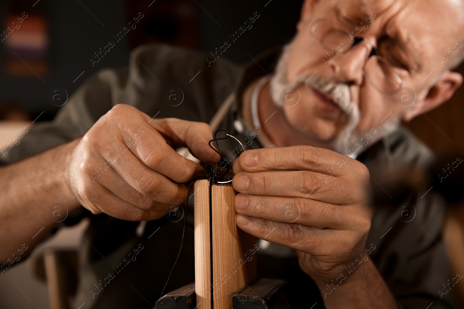 Photo of Man sewing piece of leather in workshop, closeup
