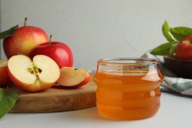 Photo of Sweet honey and fresh apples on white table, selective focus. Space for text