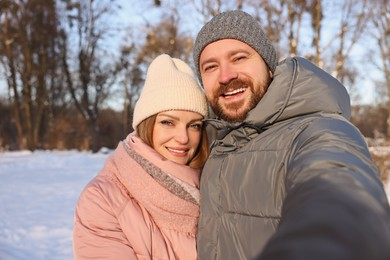 Happy couple taking selfie in sunny snowy park. Space for text