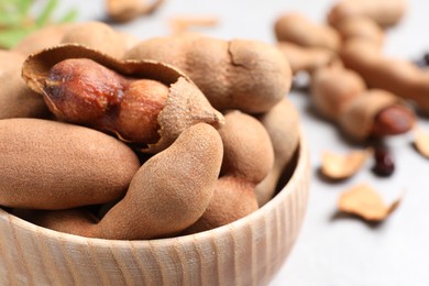 Photo of Delicious ripe tamarinds in wooden bowl on light table, closeup