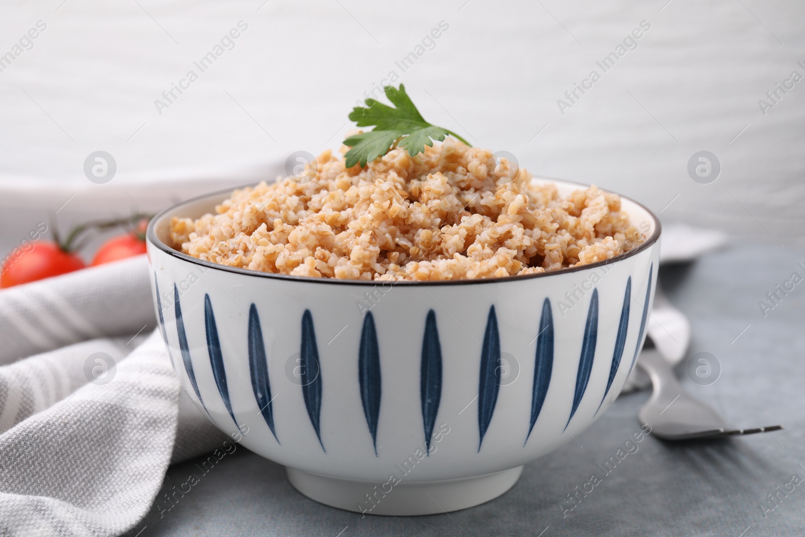 Photo of Tasty wheat porridge with parsley in bowl on grey table, closeup