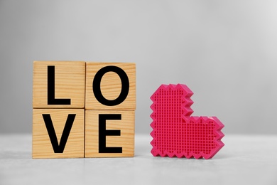 Word Love made of wooden cubes with letters near decorative heart on light table
