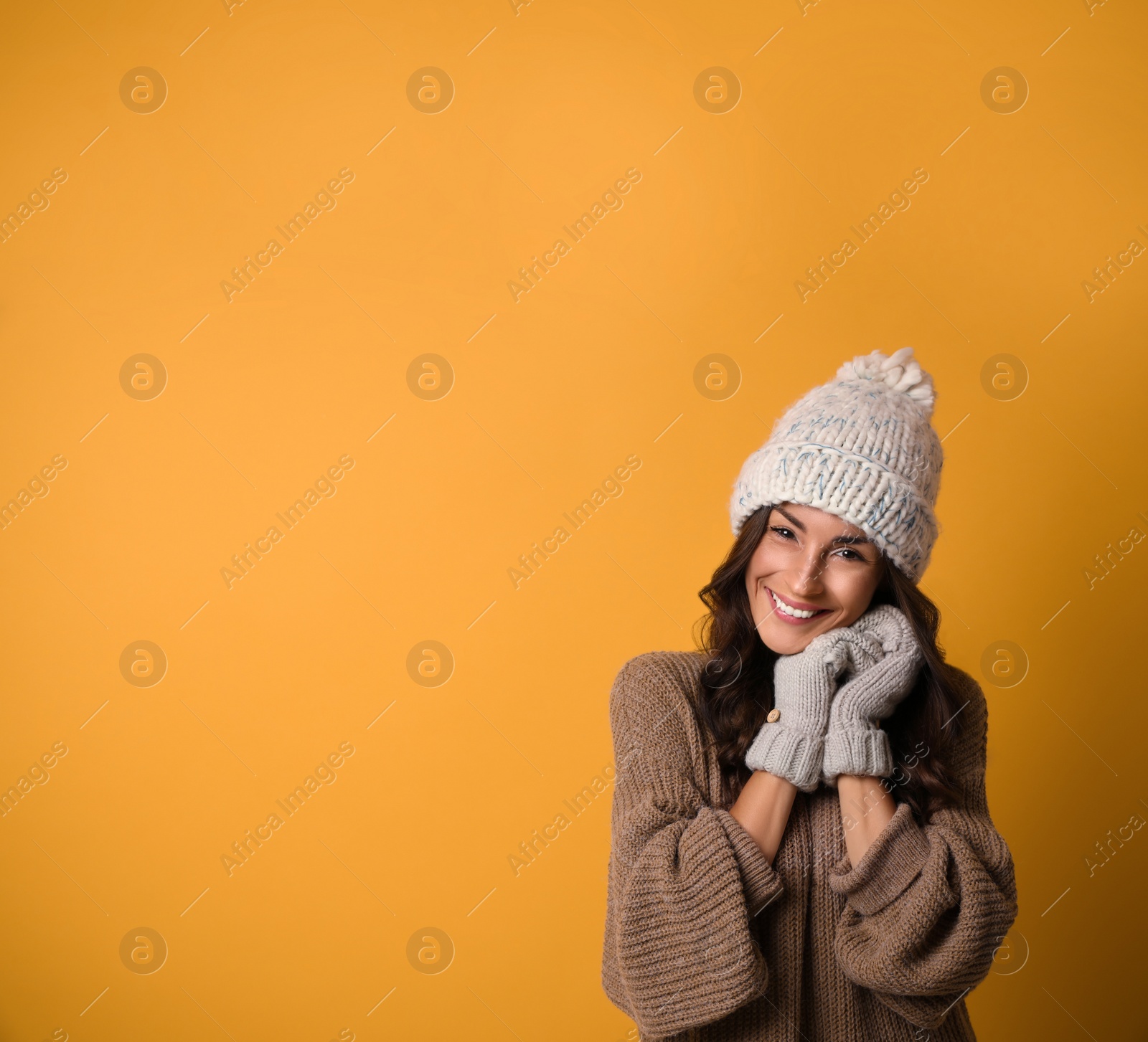 Photo of Young woman in warm sweater, hat and mittens on yellow background, space for text. Christmas season