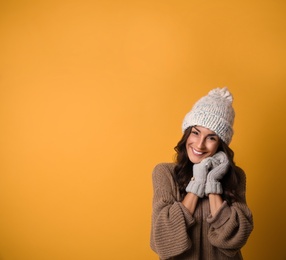Photo of Young woman in warm sweater, hat and mittens on yellow background, space for text. Christmas season