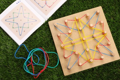 Photo of Wooden geoboard with rubber bands, activity book on artificial grass, flat lay. Educational toy for motor skills development