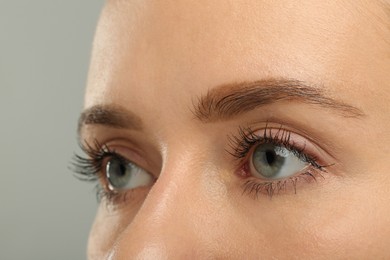 Woman with long eyelashes after mascara applying against grey background, closeup