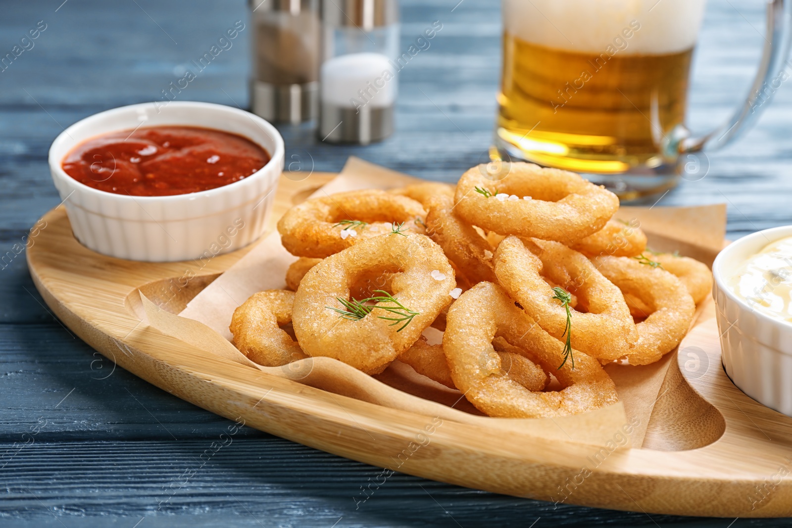 Photo of Fried onion rings served with sauces and beer on table