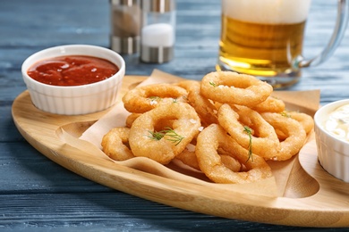 Photo of Fried onion rings served with sauces and beer on table