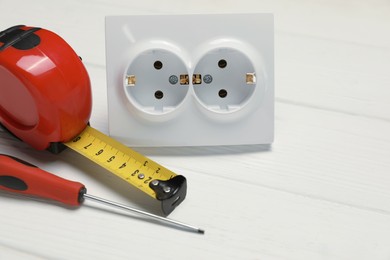 Power socket and set of electrician's tools on white wooden table, closeup