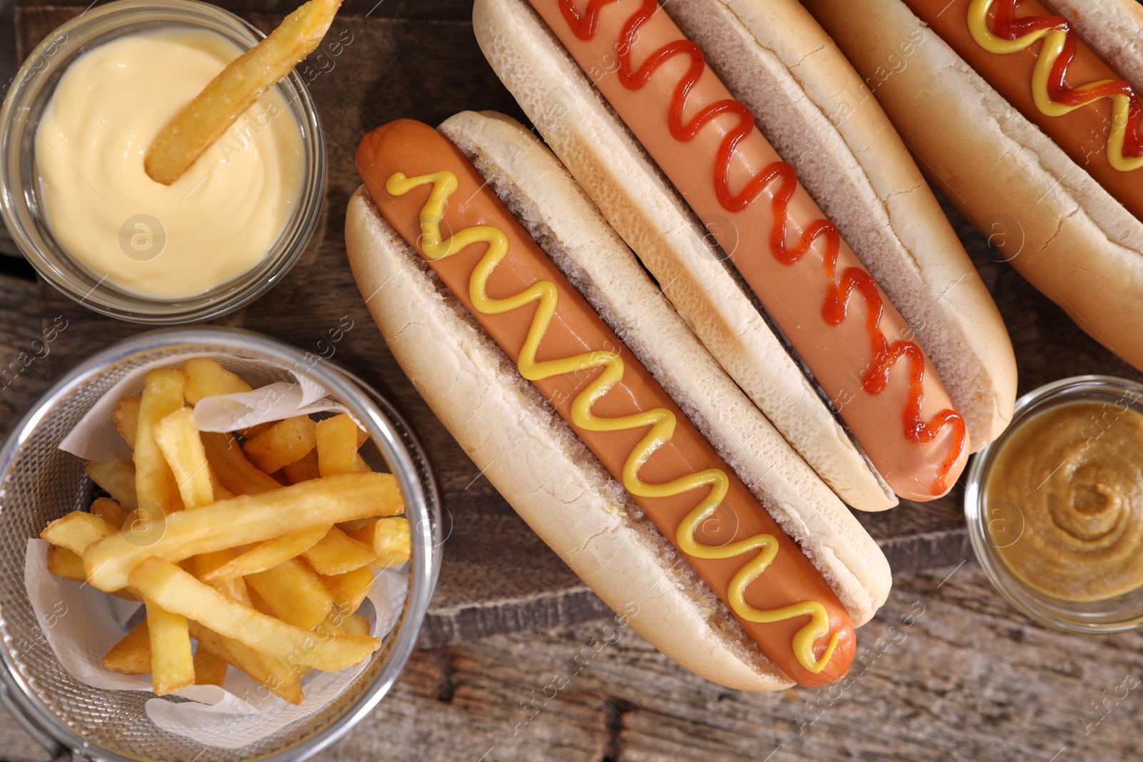 Photo of Delicious hot dogs with sauces and French fries on wooden table, top view