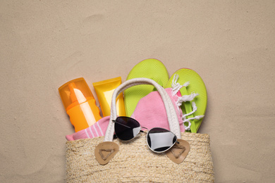 Photo of Bag with beach accessories on sand, top view