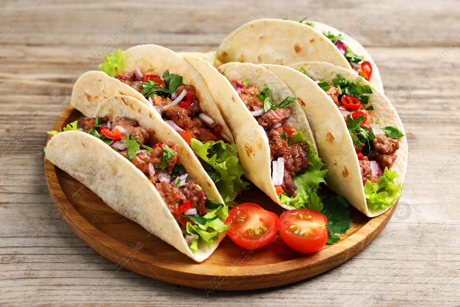 Photo of Delicious tacos with meat and vegetables on wooden table, closeup