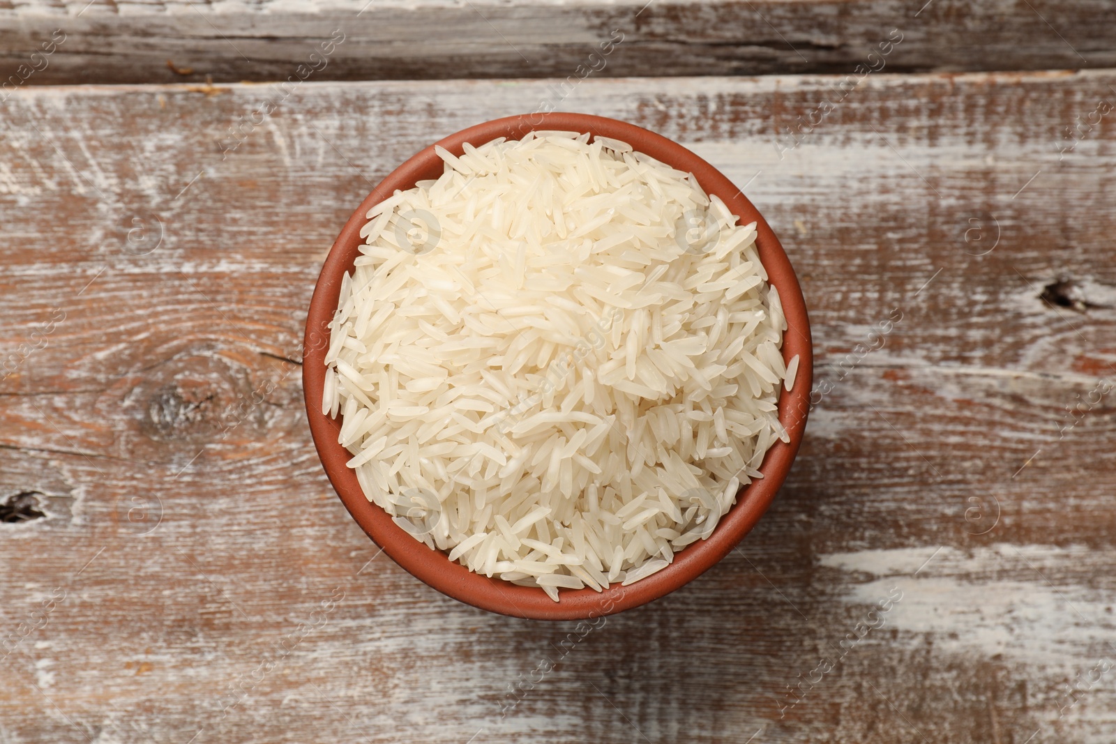 Photo of Raw basmati rice in bowl on wooden table, top view