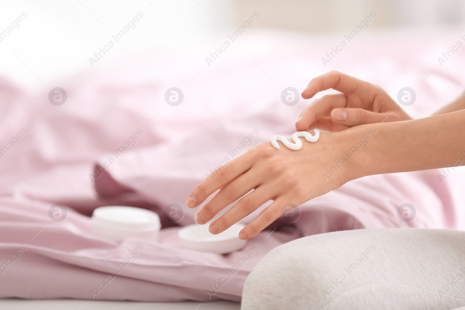 Photo of Young woman applying hand cream on bed at home