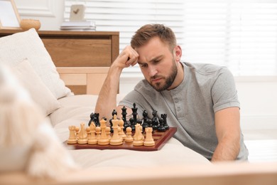 Photo of Thoughtful young man playing chess alone on sofa at home
