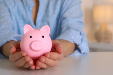 Photo of Woman with pink piggy bank at white table, closeup