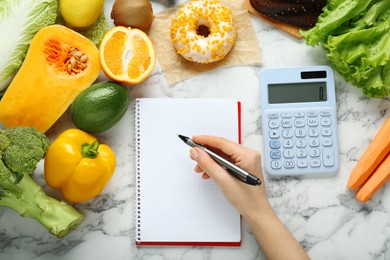 Photo of Woman calculating calories at white marble table with food products, top view. Weight loss concept