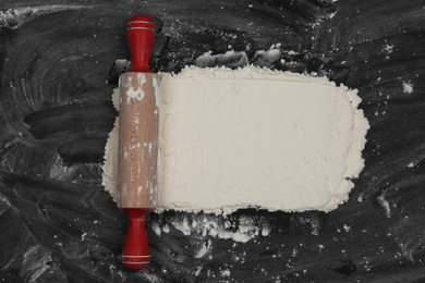 Flour and rolling pin on black table, top view. Space for text