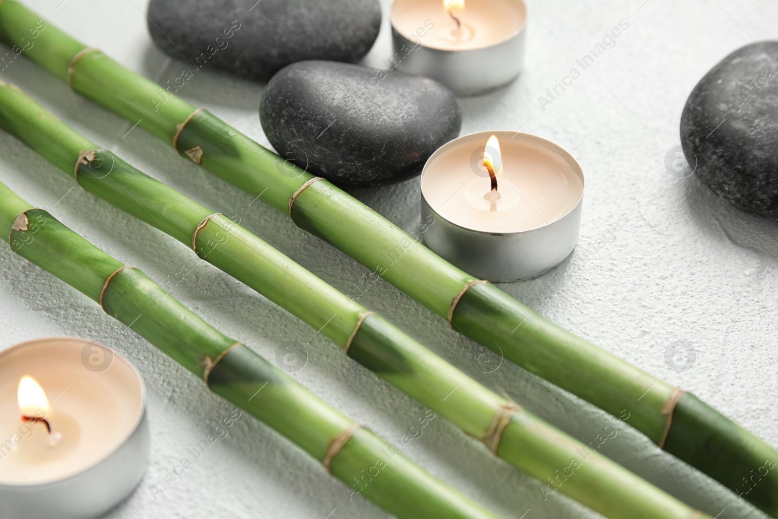 Photo of Bamboo branches, spa stones and candles on light background