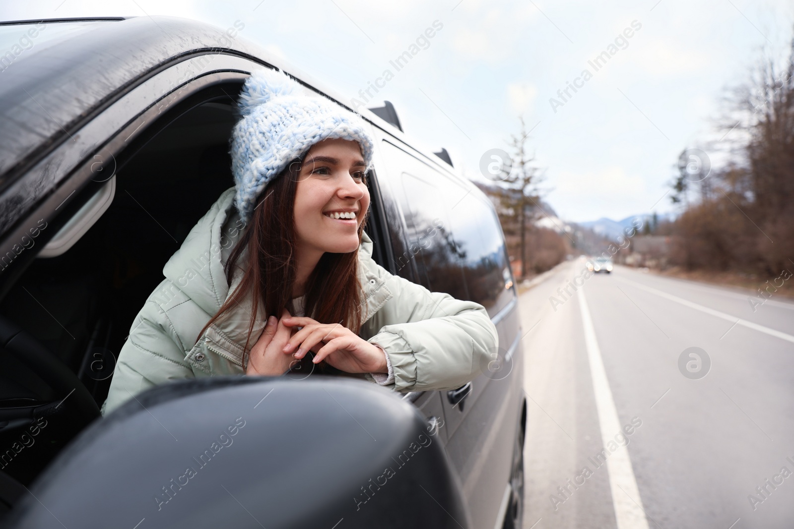 Photo of Happy woman leaning out of car window on road. Winter vacation