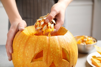 Woman making pumpkin head Jack lantern for Halloween at light table indoors, closeup