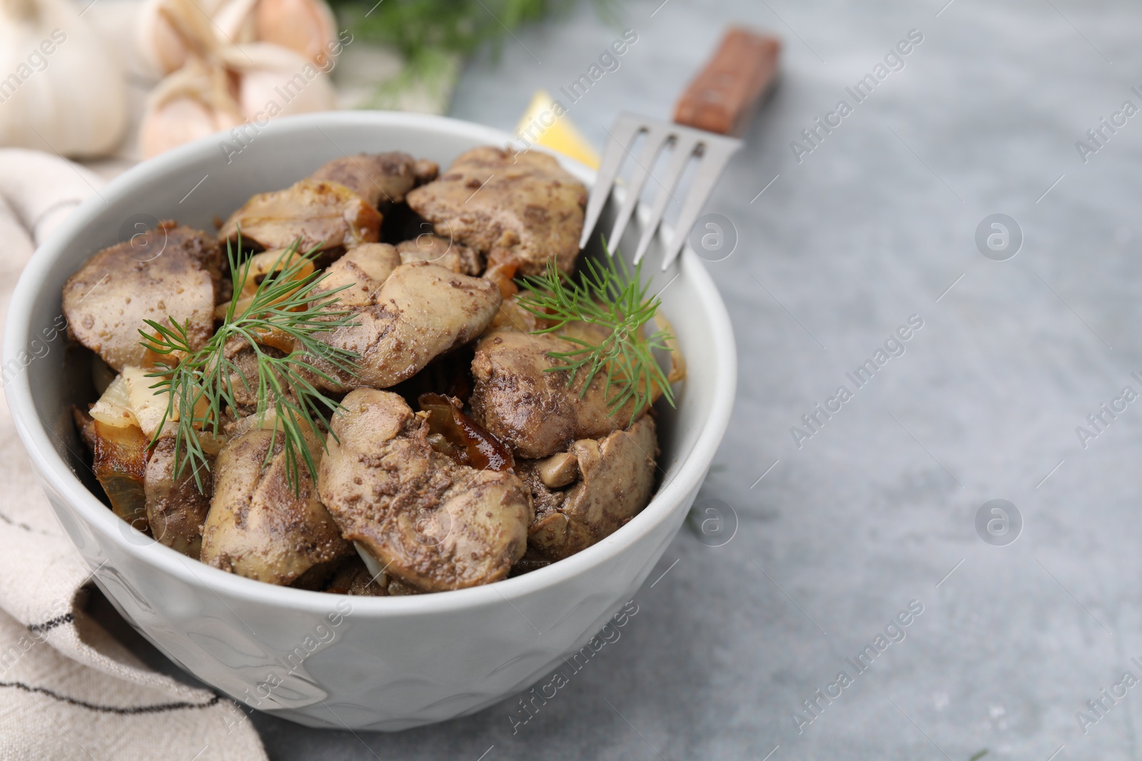 Photo of Tasty fried chicken liver with dill and fork on grey table, closeup. Space for text