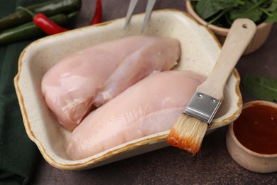 Photo of Marinade, basting brush and raw chicken fillets on brown table, closeup