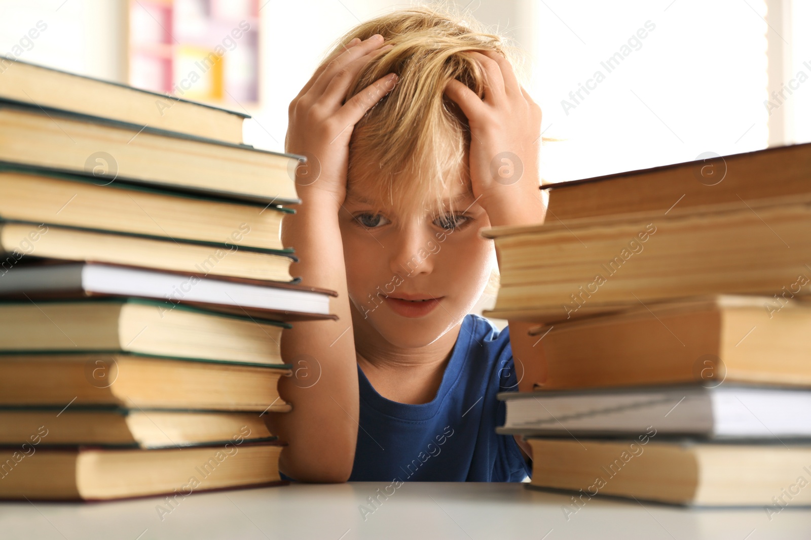 Photo of Emotional little boy at table with books. Doing homework