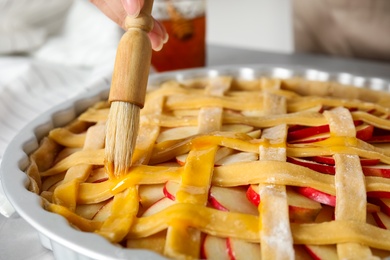 Woman applying liquid egg onto traditional English apple pie with brush at table, closeup