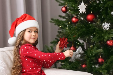 Photo of Cute girl decorating Christmas tree at home