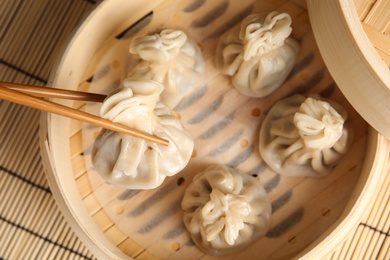 Photo of Chopsticks with baozi dumpling over bamboo steamer, closeup