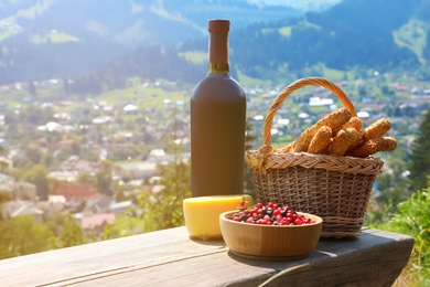Bottle of red wine and food for picnic on bench against mountain landscape