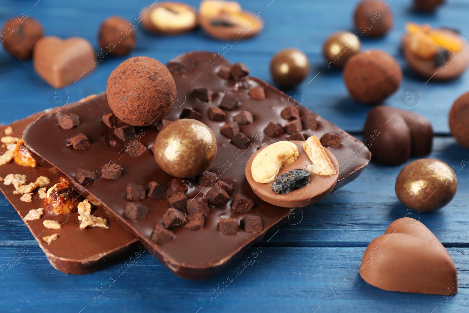 Photo of Different delicious chocolate candies and bars on blue wooden table, closeup