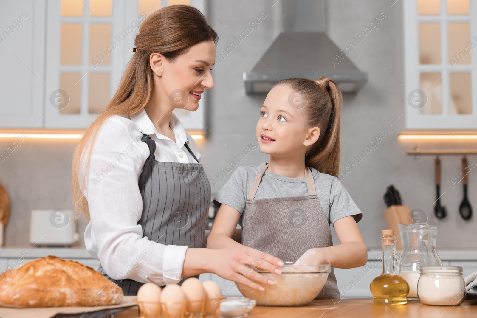 Photo of Making bread. Mother and her daughter kneading dough at wooden table in kitchen