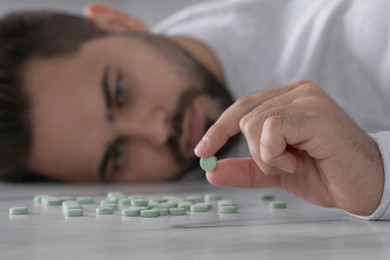 Depressed man holding antidepressant pill at white marble table, selective focus