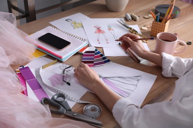 Photo of Fashion designer drawing sketch at wooden table, closeup