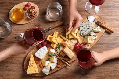 Photo of Women with glasses of wine and cheese plate on table, top view