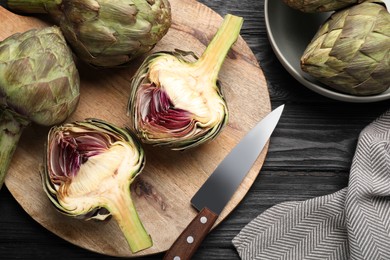 Photo of Cut and whole fresh raw artichokes on black wooden table, flat lay