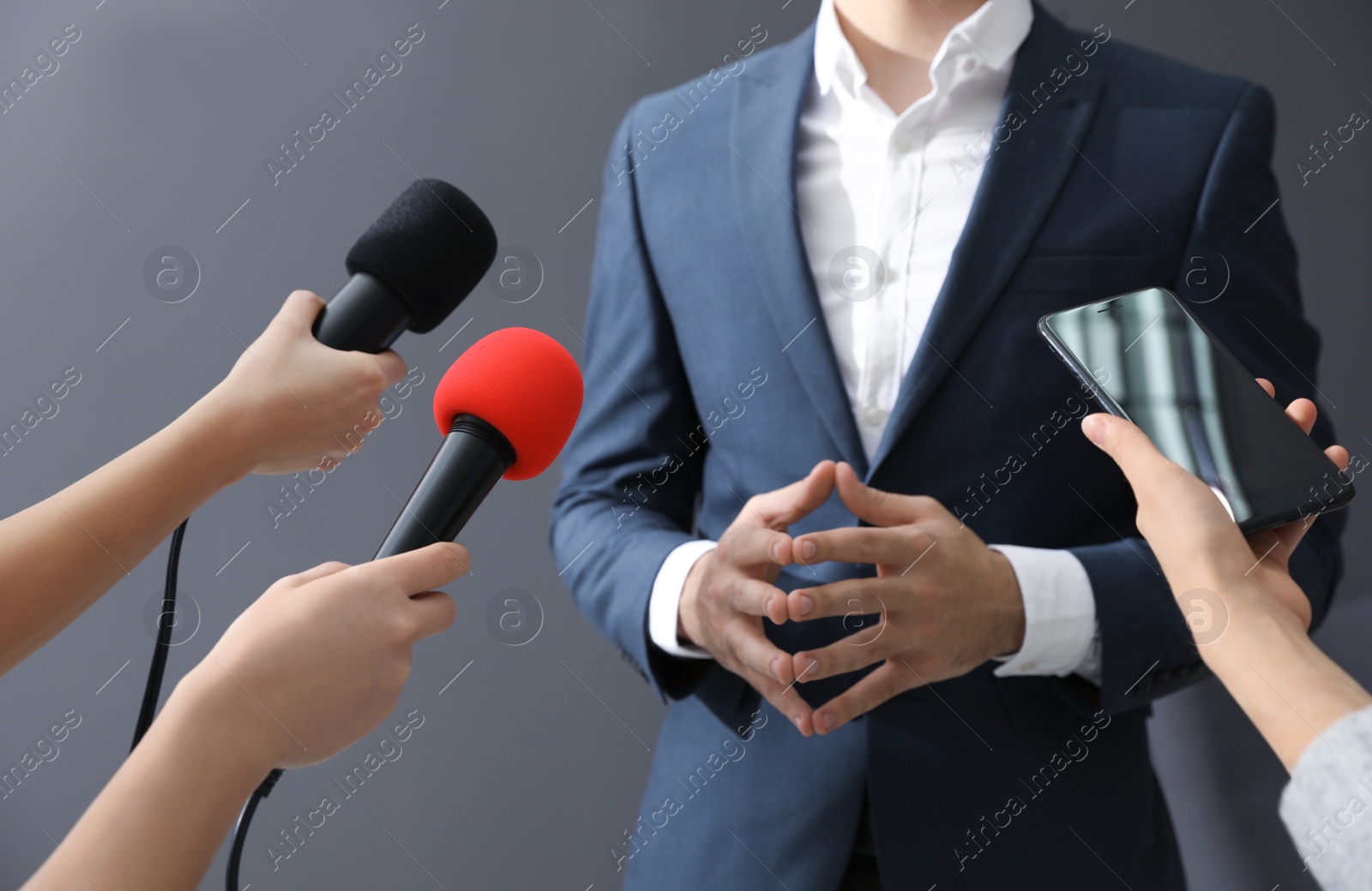 Photo of Professional journalists interviewing businessman on grey background, closeup