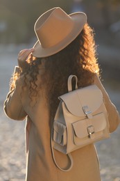 Photo of African-American woman with stylish beige backpack on city street, back view