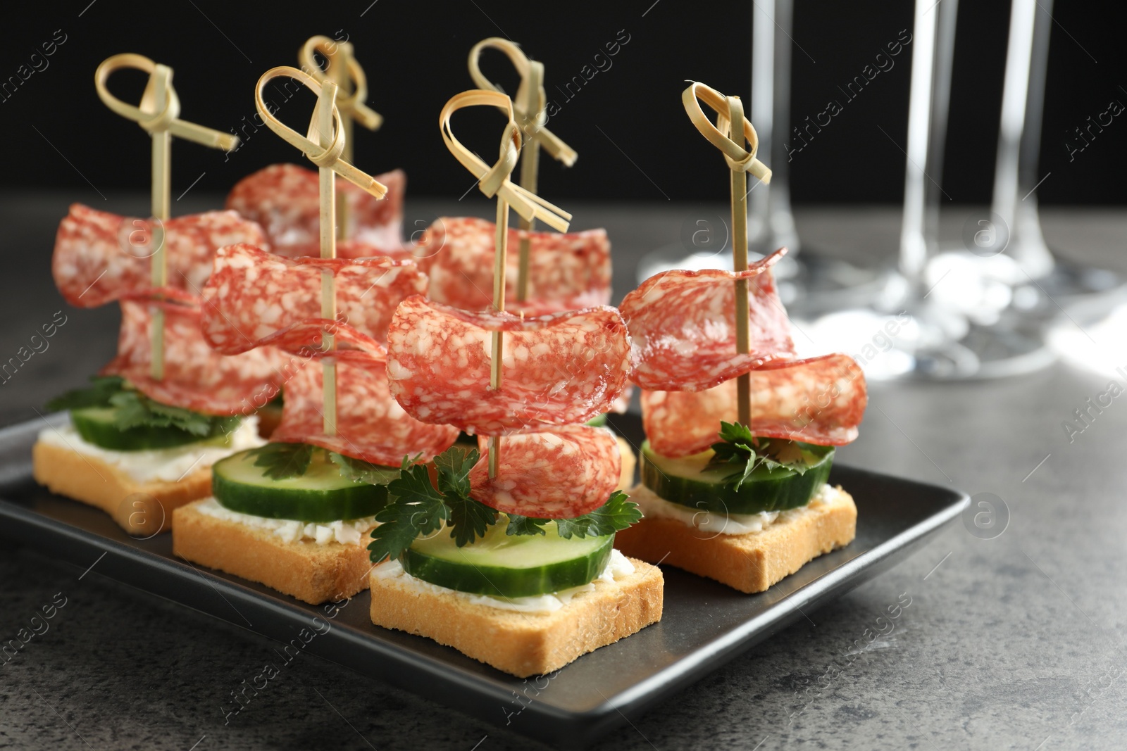 Photo of Tasty canapes with salami, cucumber and cream cheese on grey table, closeup