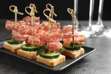 Photo of Tasty canapes with salami, cucumber and cream cheese on grey table, closeup