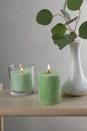 Photo of Scented candles near vase with eucalyptus branch on wooden table
