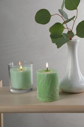 Scented candles near vase with eucalyptus branch on wooden table