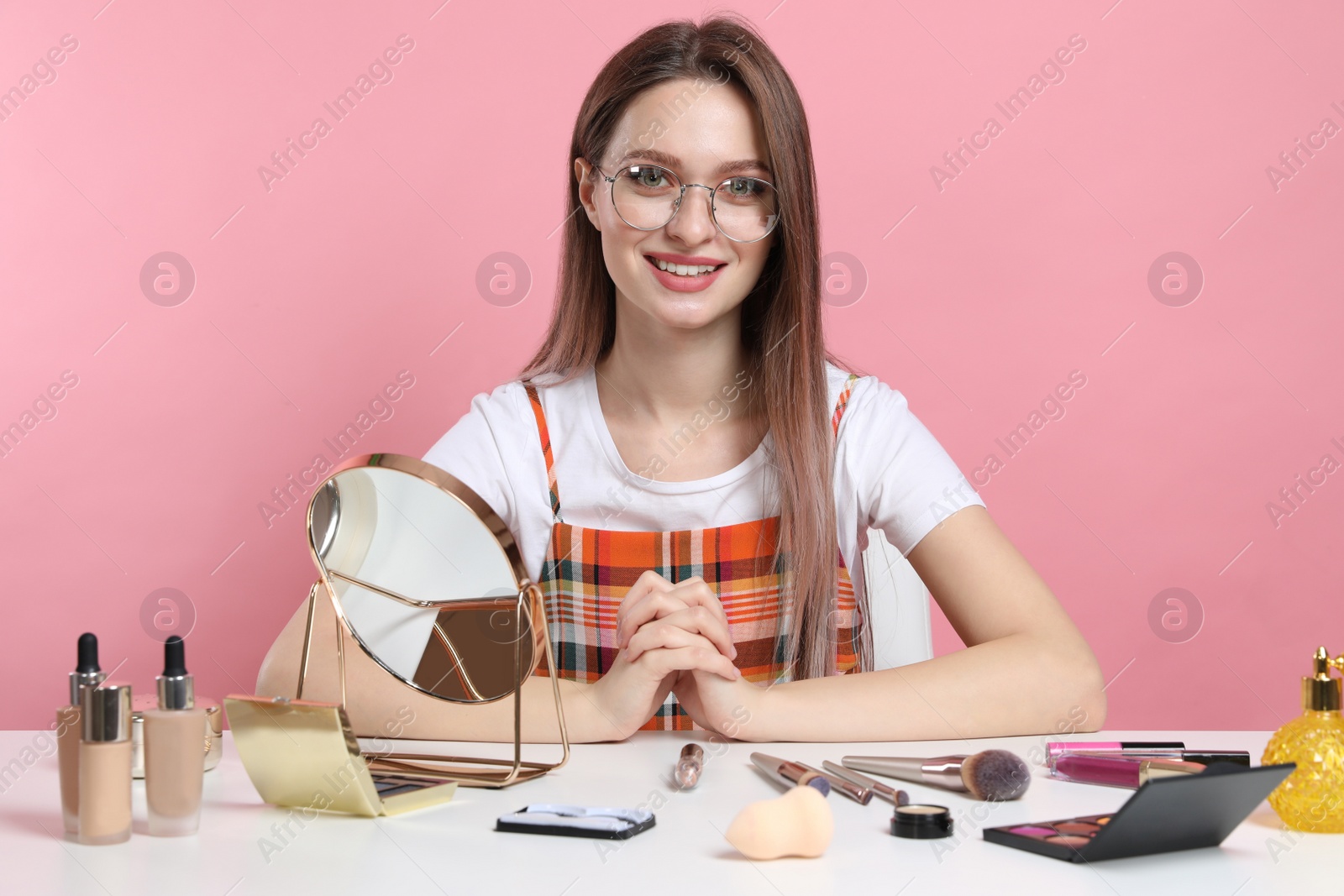 Photo of Beauty blogger at table with different cosmetic products against pink background