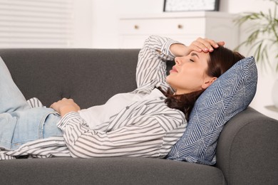 Photo of Young woman suffering from headache on sofa indoors. Hormonal disorders