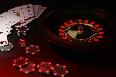 Photo of Roulette wheel with ball, chips, dice and playing cards on dark table, closeup. Casino game